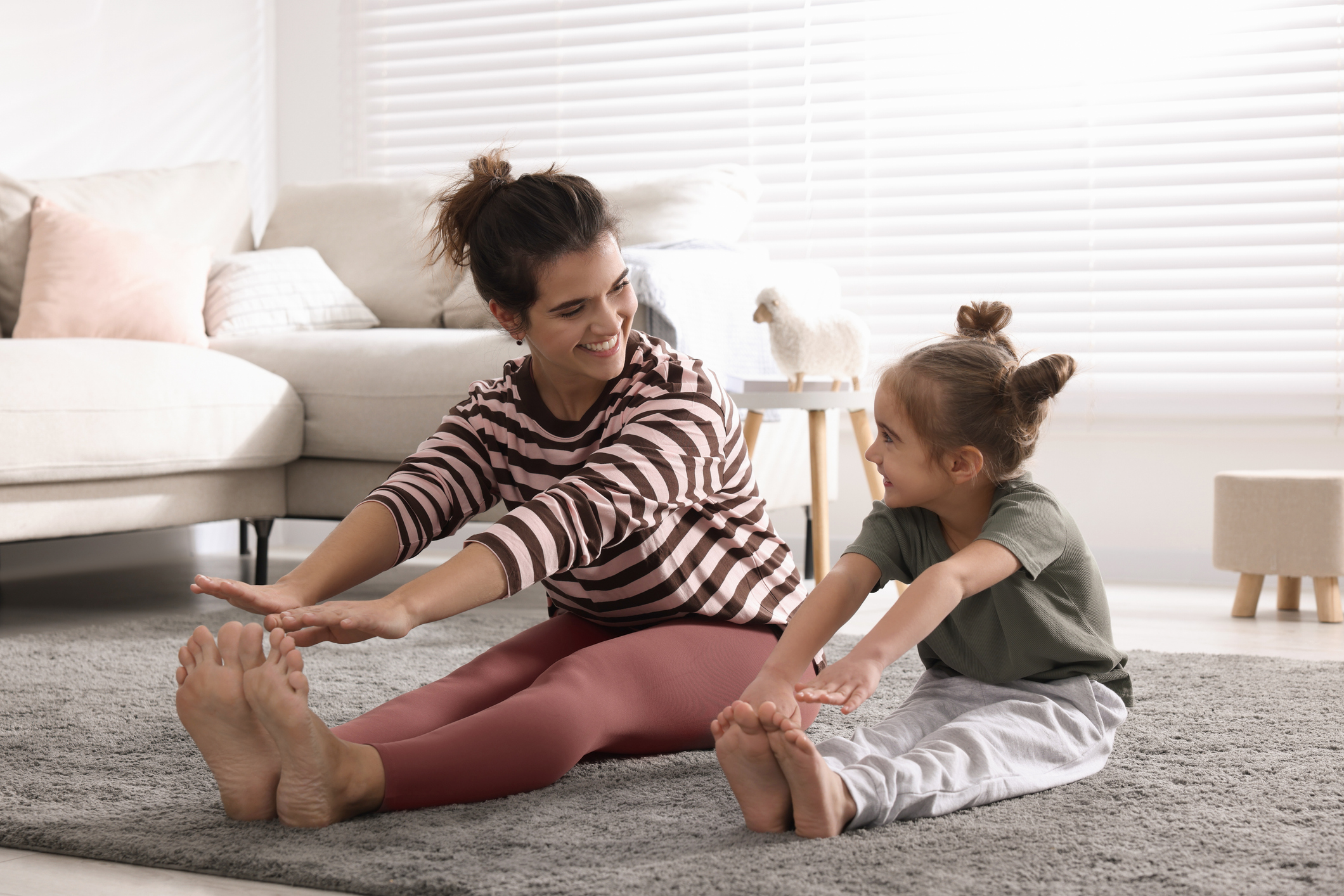 Young mother and her daughter stretching together at home